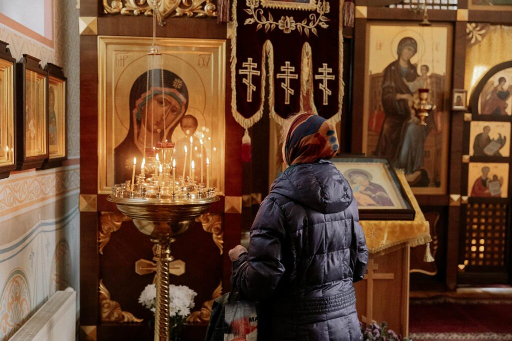 Жінка в хустці молиться та запалює свічку біля ікони Божої Матері в церкві; символічне фото до теми Страсної п'ятниці та скорботи