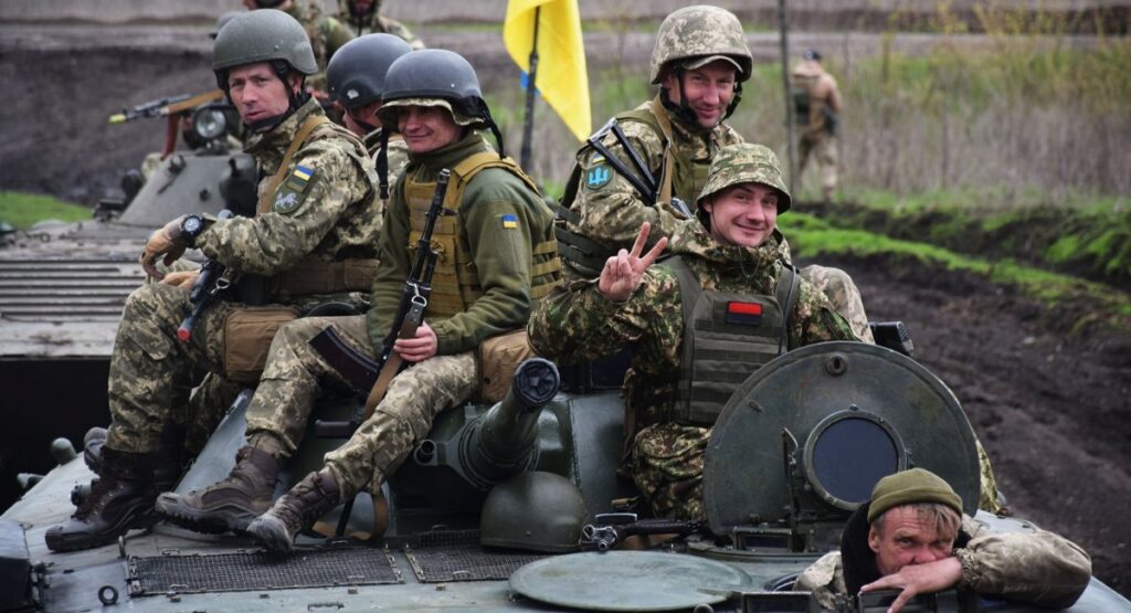 Група українських військових у камуфляжі та шоломах на броні танка з державним прапором; воїни 1-ї окремої танкової Сіверської бригади до Дня піхоти.