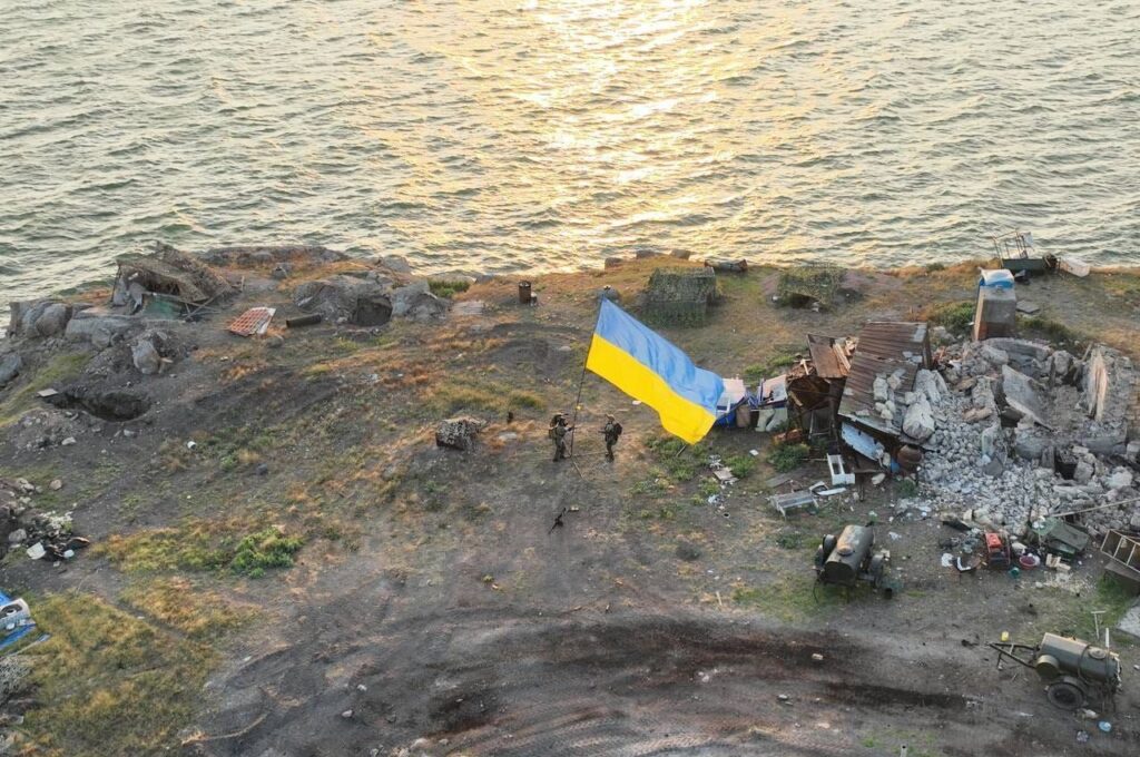 Панорамний знімок зверху: українські військові встановлюють великий синьо-жовтий прапор України на кам'янистому березі звільненого острова Зміїний