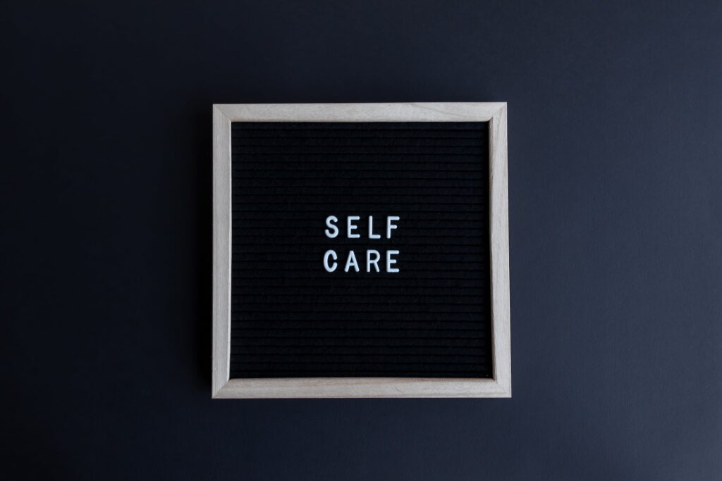 Self-Care Квадратна чорна дошка для написів у світлій дерев'яній рамці.На поверхні дошки білими пластиковими літерами викладено англійський напис «SELF CARE».