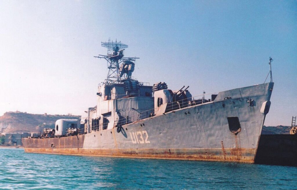 Військовий сторожовий корабель сірого кольору з бортовим номером «U132» на передньому плані, що стоїть на воді.